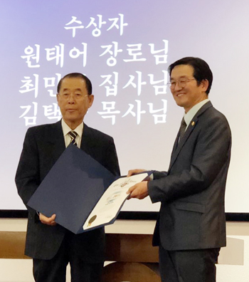 원태어 장로(왼쪽)에게 김회창 목사(오른쪽)가 표창을 대신 전달하고 있다.