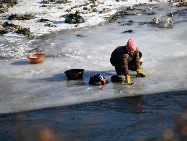 얼어붙은 강에서 빨래를 하고 있는 한 여성.
