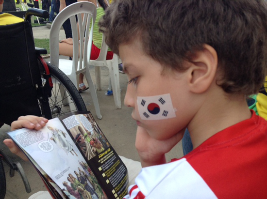 축구경기 관람을 위해 어린이가 경기장을 찾았다. 태극기를 볼에 그리고 성경의 핵심적인 내용이 담긴 만화를 눈여겨 보고 있다.