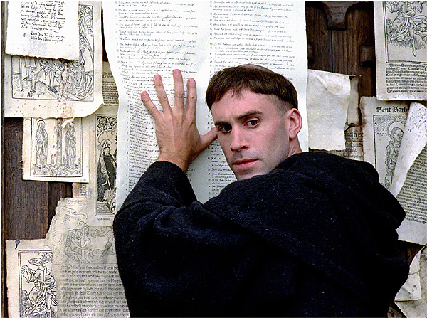 지난 2003년에 개봉된 영화 '루터'(Luther)에서 마틴 루터(조셉 파인즈 분)가 95개조 반박문을 비텐베르크 성곽 교회에 붙이고 있다.  ©영화 '루터'(Luther) 스틸 컷